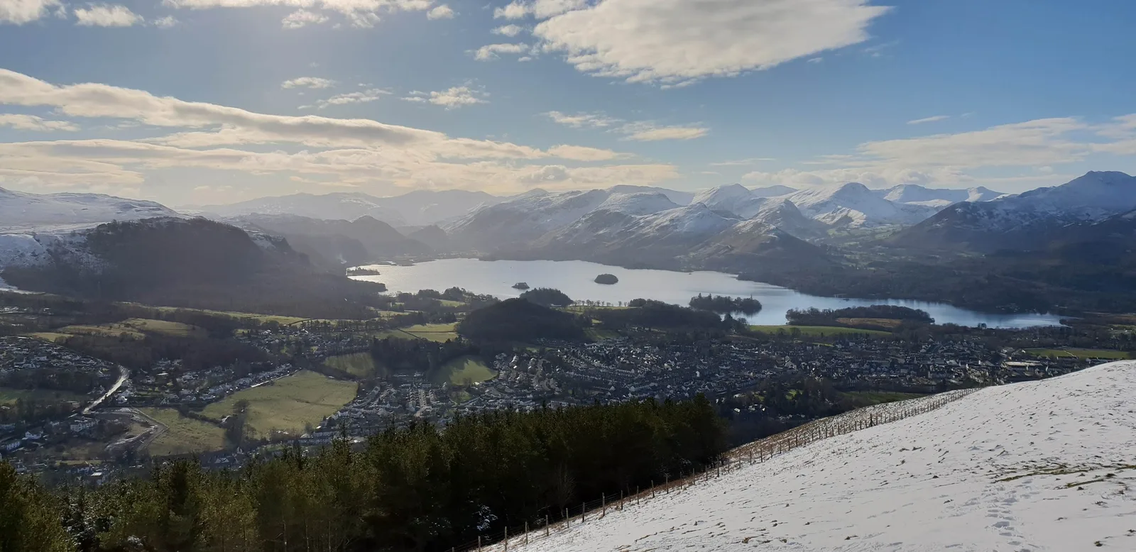 A runner on the friendly grassy summit of Latrigg with Derwentwater and the Borrowdale fells below — a short, low-risk first fell above Keswick